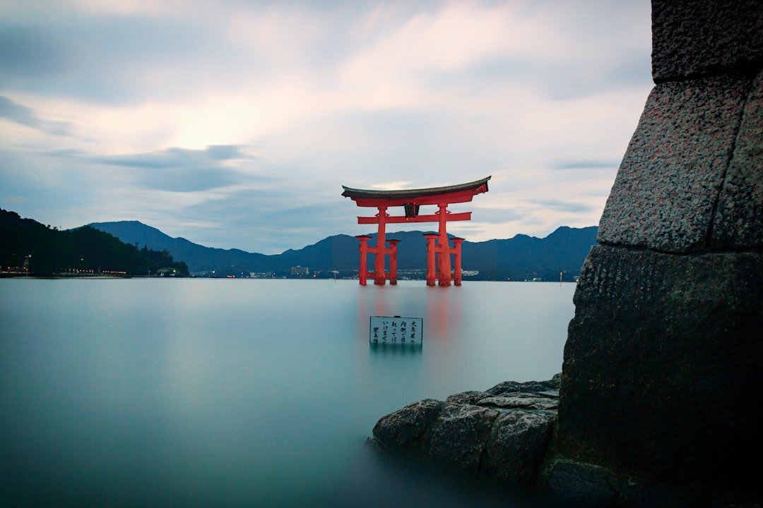 Miyajima'da Itsukushima Tapınağı'nın denizde duran kırmızı büyük torii kapısı, arkada dağlar