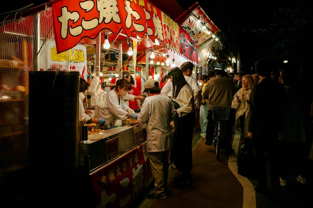Gece ışıklı bir takoyaki tezgâhının önünde sıra bekleyen insanlar