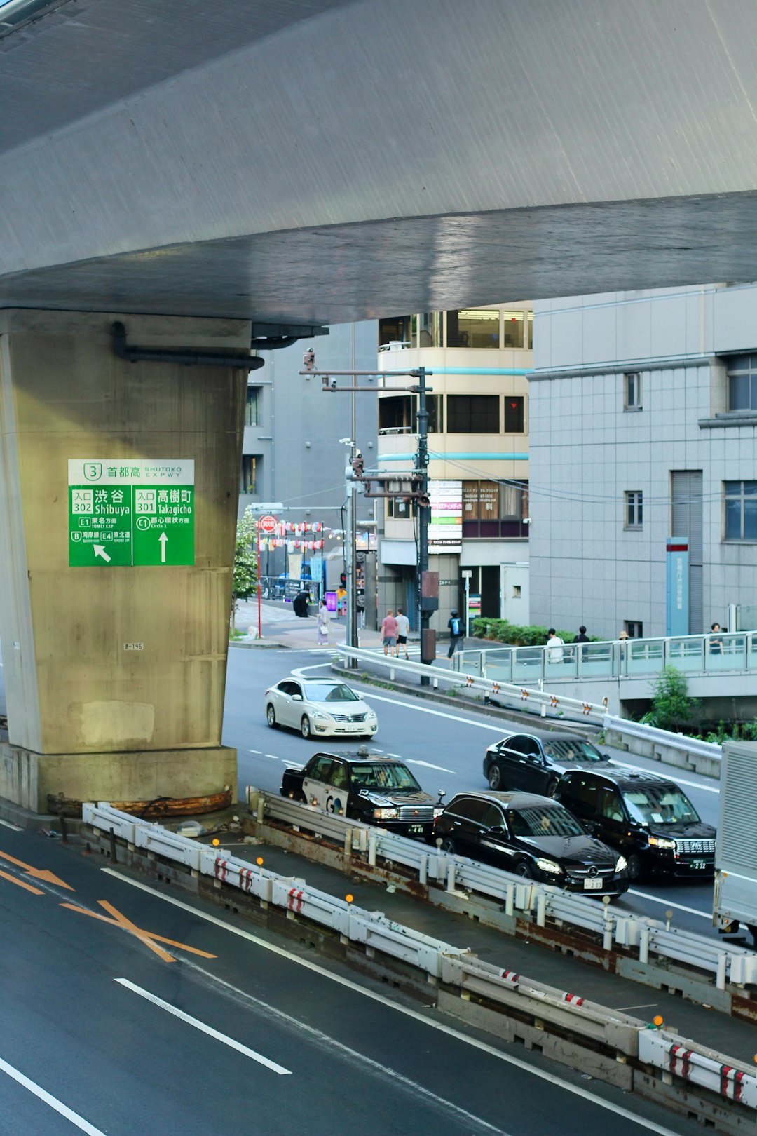 Tokyo'da şehir otoyolunun altındaki yolda araç trafiği ve yeşil yön tabelası