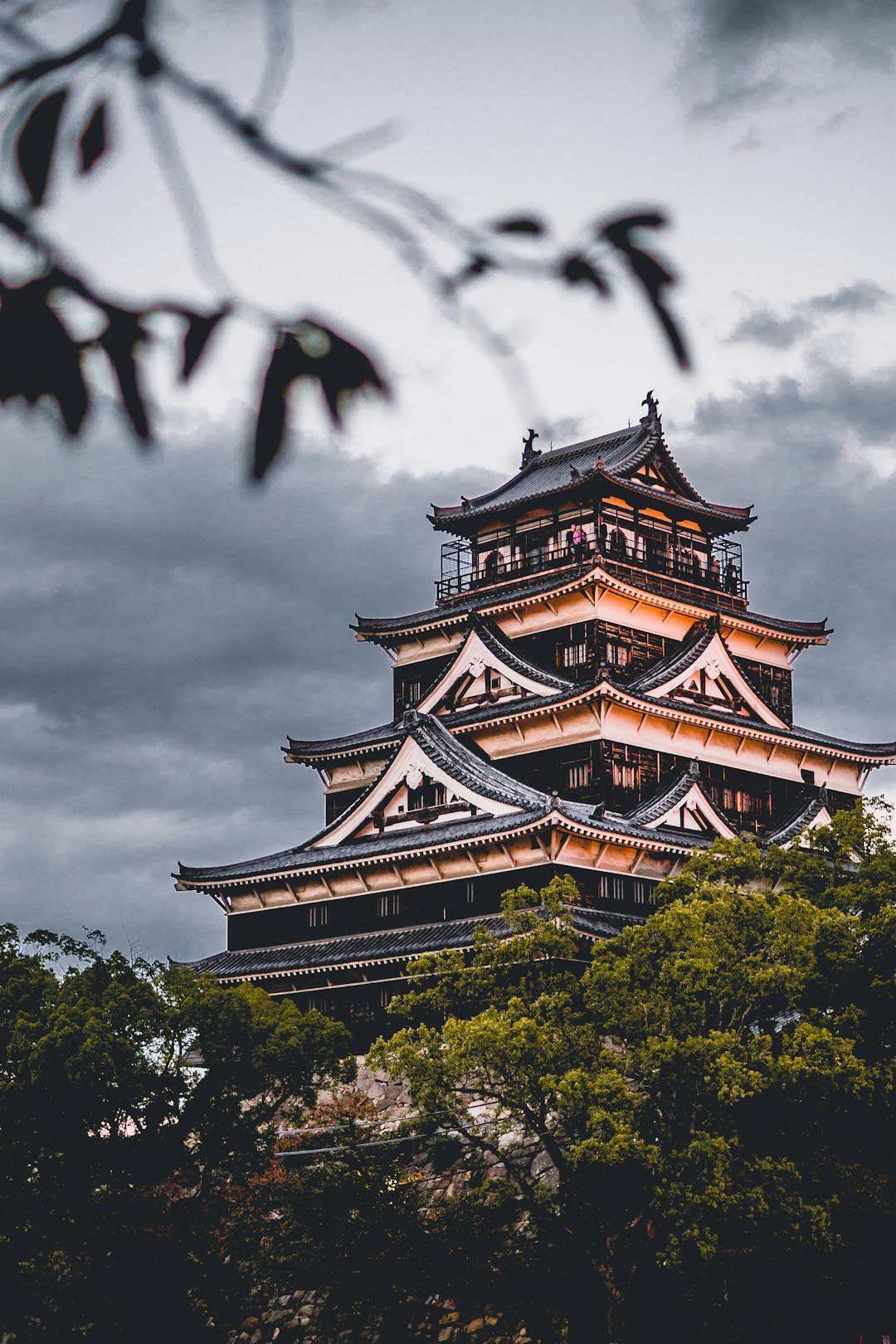 Yeşil ağaçların üstünde yükselen bulutlu gökyüzü altında Hiroshima Kalesi