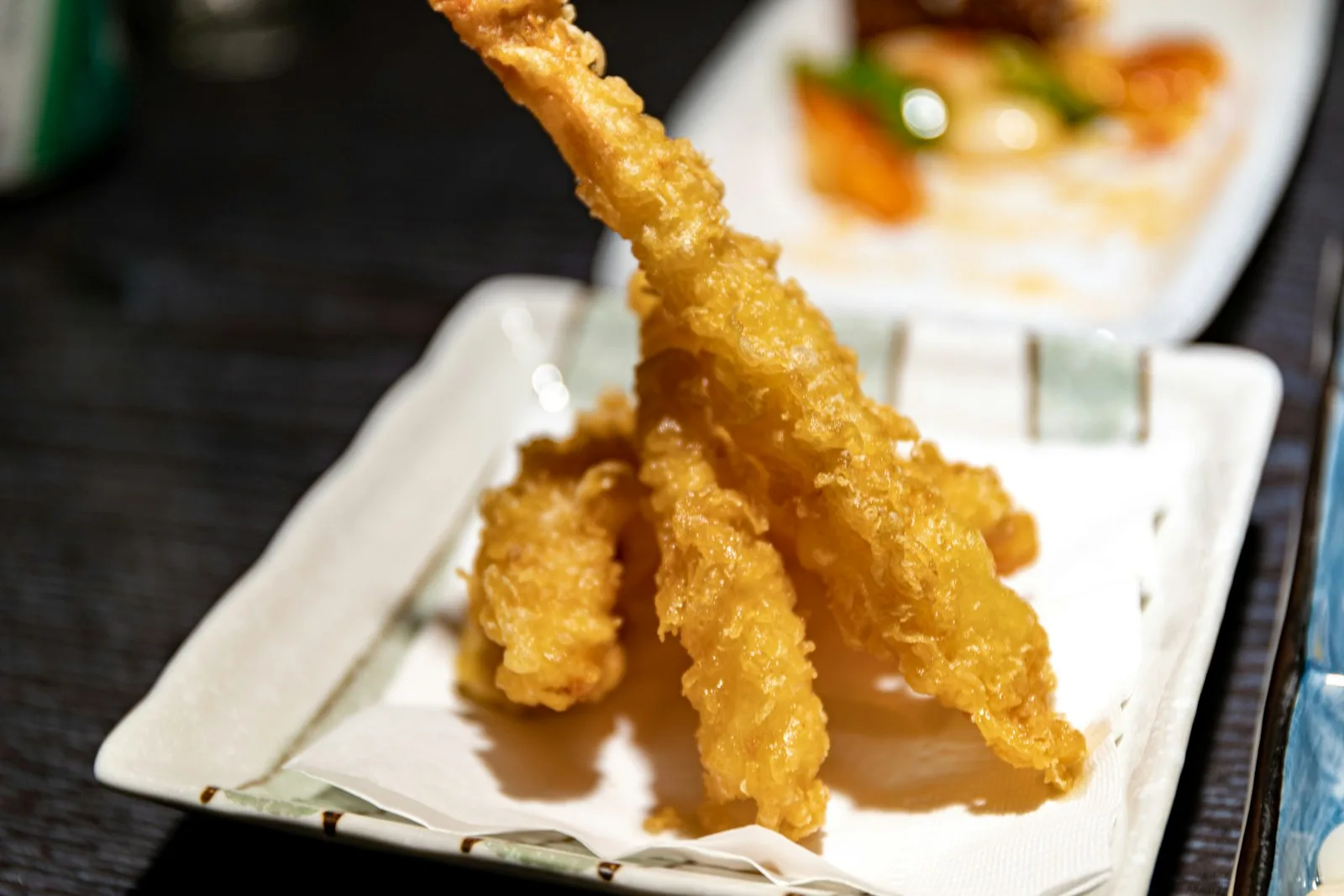 Kağıt serilmiş beyaz tabakta üç parça altın renkli, çıtır tempura