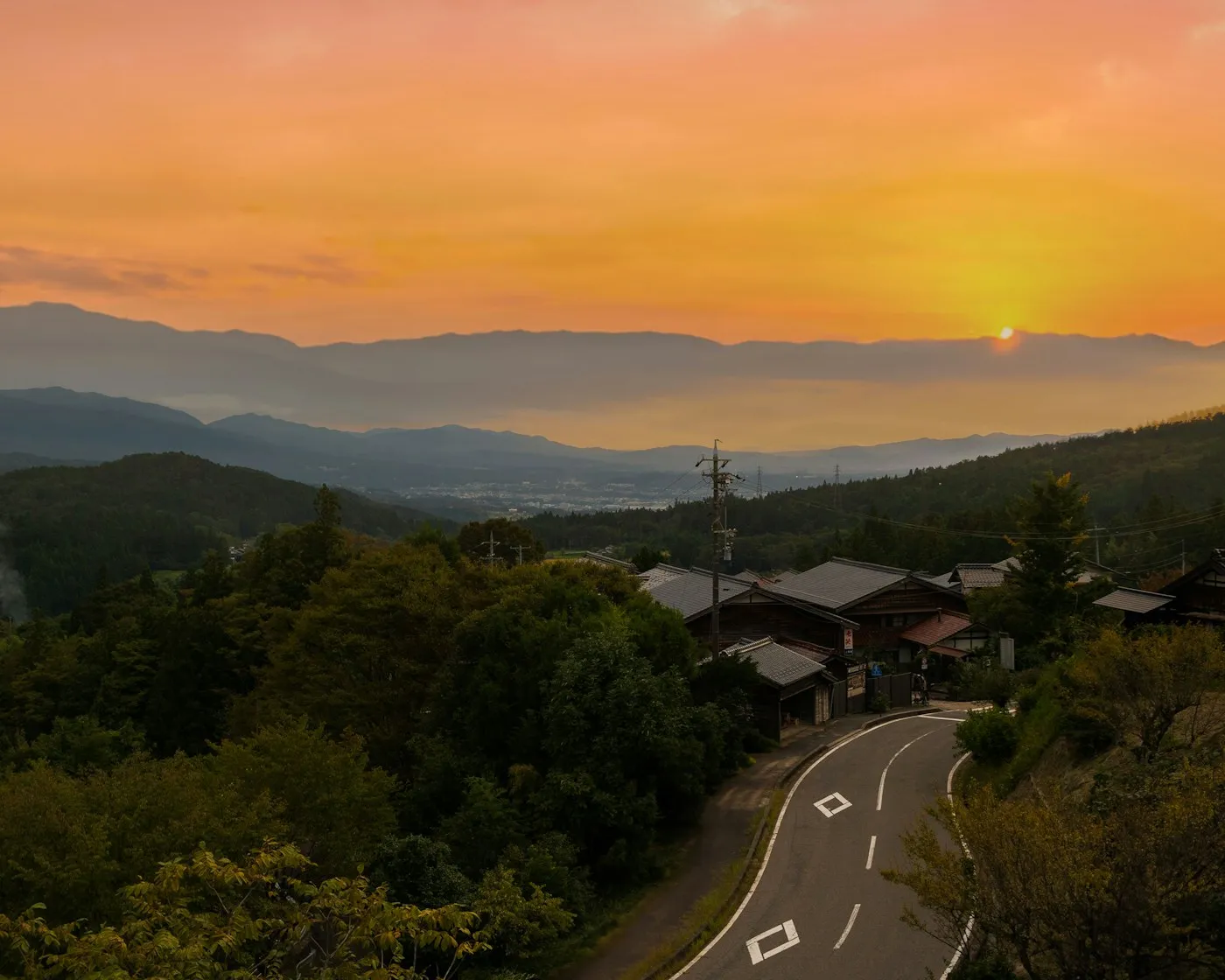 Gün batımında ormanlı tepelerden kıvrılan yol ve uzak dağlar