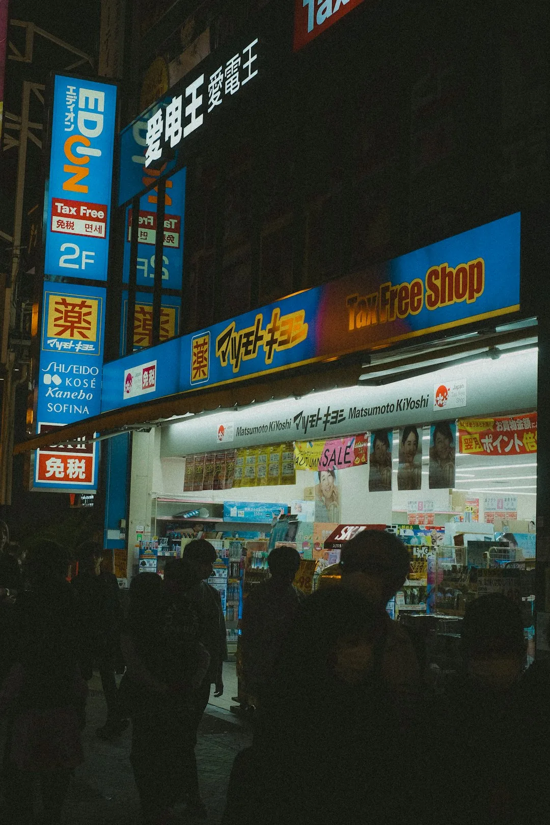 Osaka'da gece parlak ışıklı bir Matsumoto Kiyoshi eczane mağazasının önünden geçen yayalar