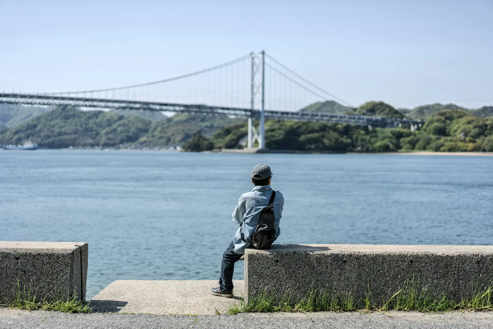 Shimanami Kaido'da bir asma köprüye bakarak kıyıda oturan kişi