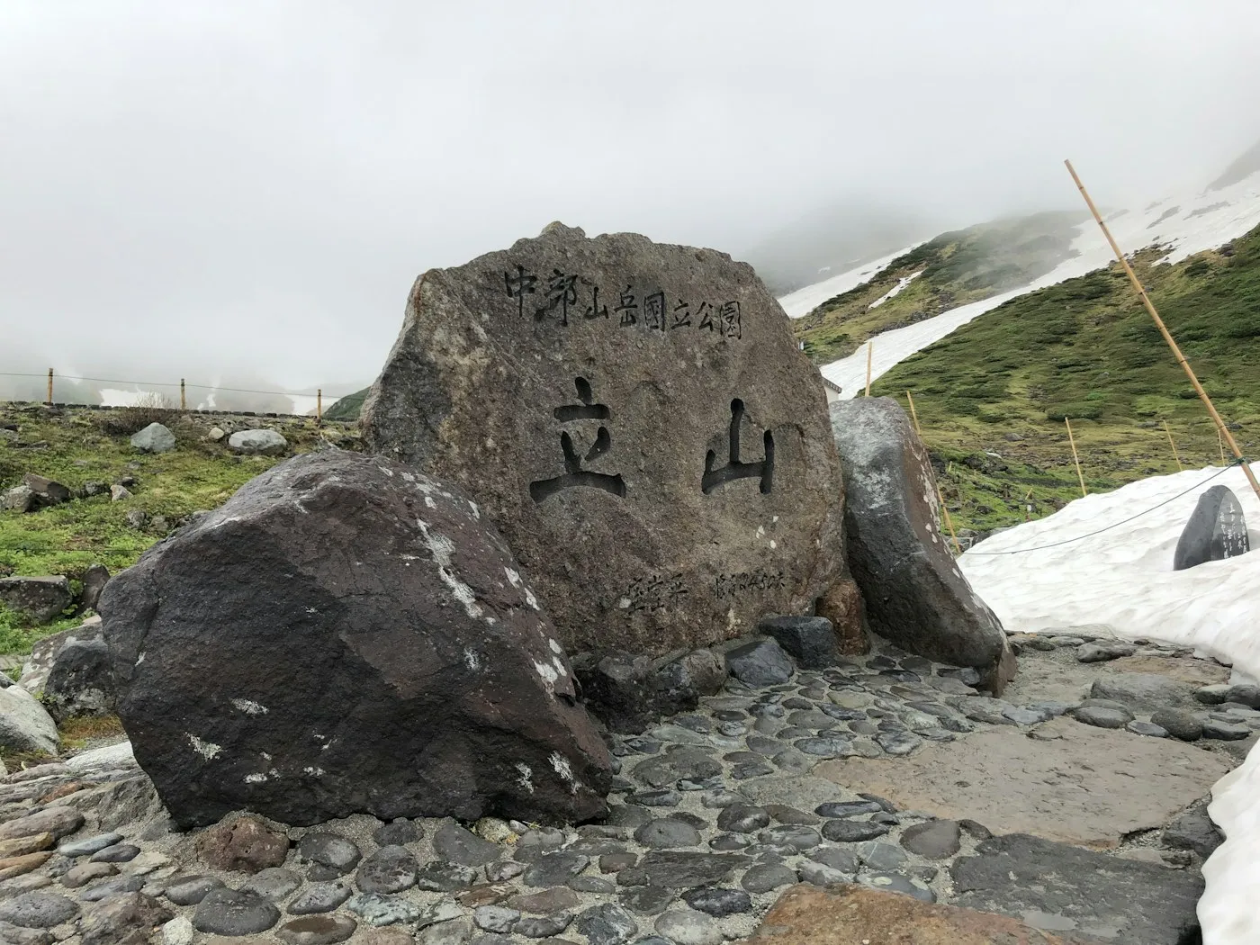 Üzerinde Tateyama yazan büyük bir kaya ve karlı tepeler